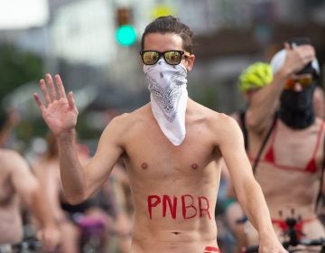 A rider waves to approving pedestrians who stopped to watch the Philly Naked Bike Ride make its way through Center City. (Jonathan Wilson for WHYY)
