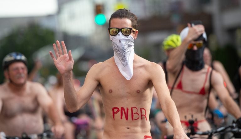 A rider waves to approving pedestrians who stopped to watch the Philly Naked Bike Ride make its way through Center City. (Jonathan Wilson for WHYY)