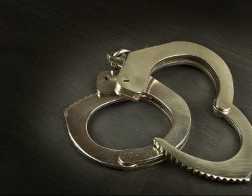 Metal police handcuffs on a dark wooden board.