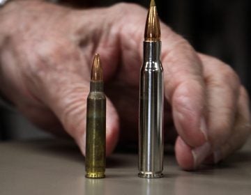 Bob Viden, owner of Bob's Little Sport Shop in Glassboro N.J., compares the bullets used in the AR 15 (left) and the Remmington hunting rifle. (Emma Lee/WHYY)