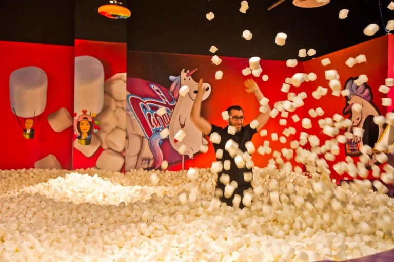 Adults play in the 'highly instagrammable' marshmallow pit at the Fashion District's Candytopia exhibit. (Kimberly Paynter/WHYY)