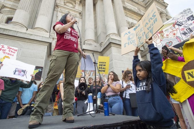 Sarina Mahmud holds a sign aloft as Philadelphia City Councilmember Helen Gym addresses the crowd. (Jonathan Wilson for WHYY)