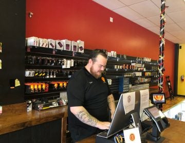 Tyler Wilson, assistant manager at Unreal Vapors near Newport, Del., rings up an order for a lemonade-flavored e-cigarette fluid. (Cris Barrish/WHYY)