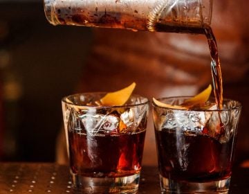 A bartender pours a cocktail into glasses with ice cubes. (iStock)