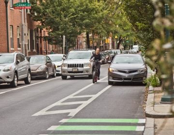 A bicyclist riders in a Center City bike lane, swerving to avoid a car parked improperly in the lane. (Kimberly Paynter/WHYY)