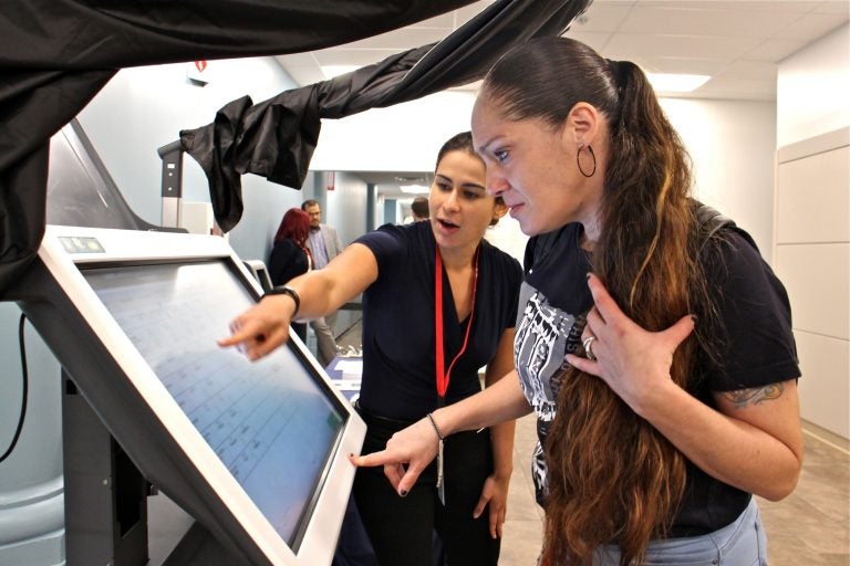 Diane Duffin learns how to use a voting machine with the help of Michelle Montalvo of the City Commissioners Office. Duffin registered to vote for the first time after learning that a conviction did not prevent her from voting in Pennsylvania. (Emma Lee/WHYY)