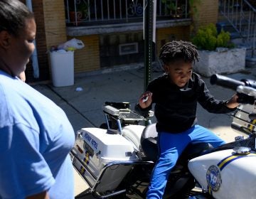 Octavia Abney watches her son Dylan, 4, sit on a Philadelphia Police Department motorbike during the Love Peace and Soul Fest block party on Sunday October 5, 2019 at the site of the August Police shooting and stand off in the Nicetown-Tioga section of Philadelphia. (Bastiaan Slabbers for WHYY)