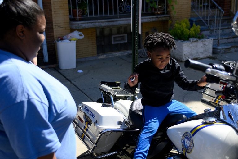 Octavia Abney watches her son Dylan, 4, sit on a Philadelphia Police Department motorbike during the Love Peace and Soul Fest block party on Sunday October 5, 2019 at the site of the August Police shooting and stand off in the Nicetown-Tioga section of Philadelphia. (Bastiaan Slabbers for WHYY)