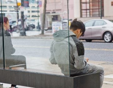 A commuter listens to music while they wait for a SEPTA bus. (Kimberly Paynter/WHYY)