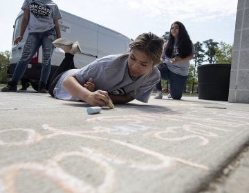 Sophomore Fatima Saldana, 16, works on her message as National Children's Mental Health Awareness Day is celebrated with students participating in Messages of Hope, which had them writing positive messages in chalk by the school entrance Thursday, May 10, 2018, at Oakcrest High School in Mays Landing, N.J. (Matthew Strabuk/The Press of Atlantic City via AP)