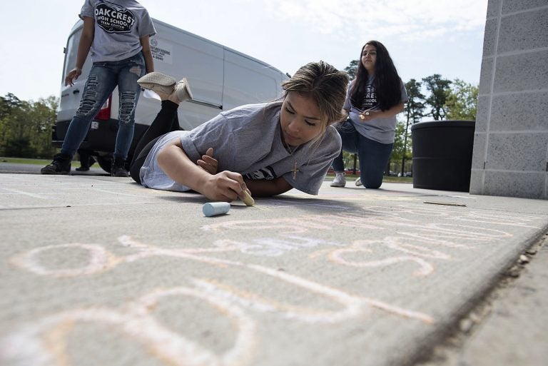 Sophomore Fatima Saldana, 16, works on her message as National Children's Mental Health Awareness Day is celebrated with students participating in Messages of Hope, which had them writing positive messages in chalk by the school entrance Thursday, May 10, 2018, at Oakcrest High School in Mays Landing, N.J. (Matthew Strabuk/The Press of Atlantic City via AP)