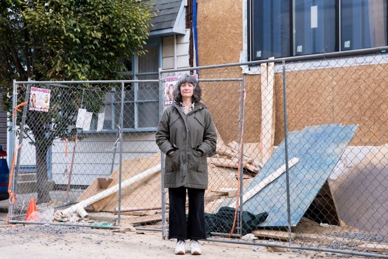 Sara Gallo stands between her home and the new construction next door on November 5, 2019. Due to the demolition and rebuilding of the twin house adjoining hers, her home now suffers structural issues, settling, and leaking. (Rachel Wisniewski for WHYY)