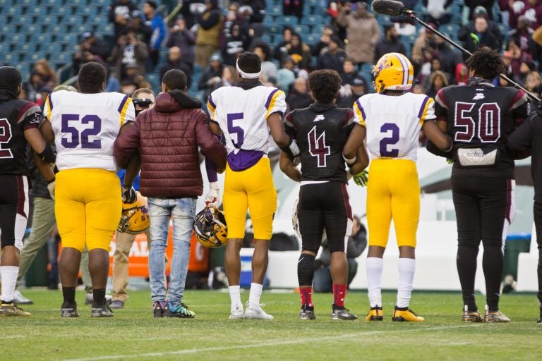 Members of the Camden Panthers and the Pleasantville Greyhounds link arms during a moment of silence for 10 year-old, Micah Tennant, who was shot during a high school football game last week. The game resumed Wednesday at Lincoln Financial field. (Kimberly Paynter/WHYY)