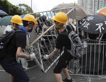 Protesters with umbrellas use steel barricades to block a road as they march through Sha Tin District in Hong Kong. (Kin Cheung/AP Photo)