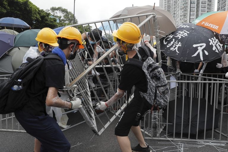 Protesters with umbrellas use steel barricades to block a road as they march through Sha Tin District in Hong Kong. (Kin Cheung/AP Photo)