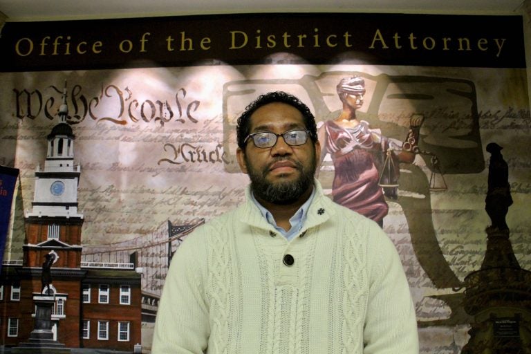 Formerly incarcerated artist James “Yaya” Hough stands in front of a mural at the Philadelphia District Attorney’s Office. (Emma Lee/WHYY)