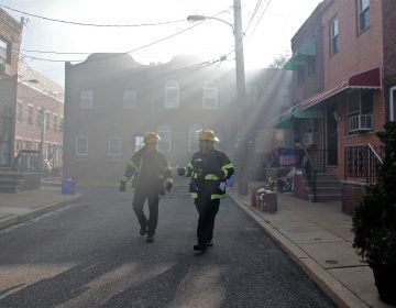 Firefighters walk through a smoke haze on South Beulah Street, checking on residents near the scene of a 3-alarm fire in the 1400 block of South 8th Street. (Emma Lee/WHYY)