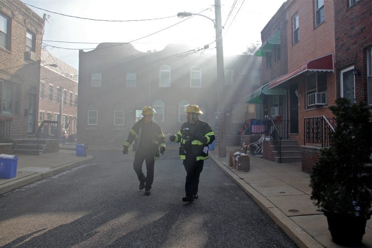 Firefighters walk through a smoke haze on South Beulah Street, checking on residents near the scene of a 3-alarm fire in the 1400 block of South 8th Street. (Emma Lee/WHYY)