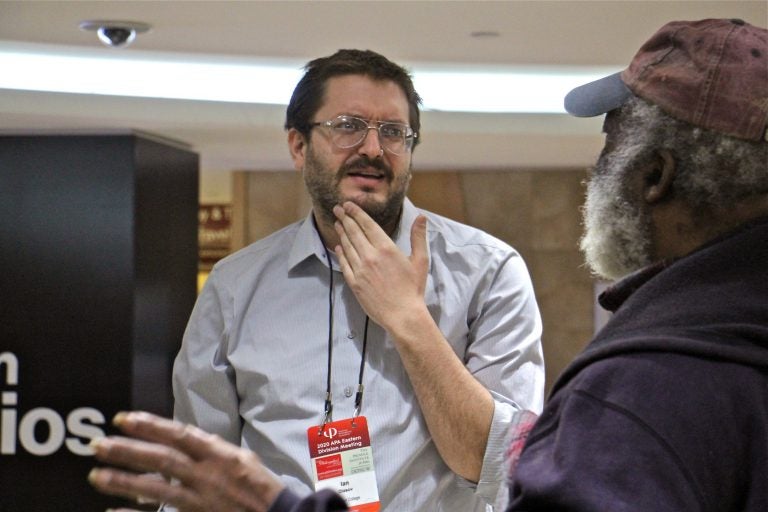 Ian Olasov (left), a part-time philosophy professor at Brooklyn College, engages with passersby at the Ask a Philosopher pop-up booth at Suburban Station in Center City. (Emma Lee/WHYY)