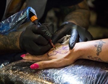 Felicia Vazquez gets a rose tattooed onto her hand by artist Ralph Fryer. (Kimberly Paynter/WHYY)