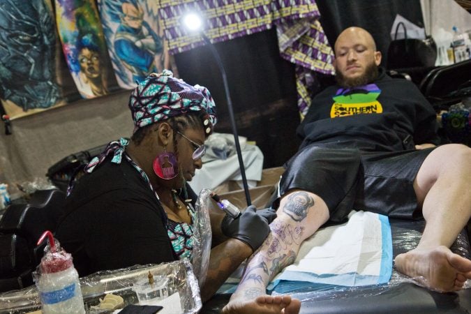 Elisheba Israel Mrozik tattoos a cobra and skull on Gil Goodman. Both traveled from Nashville to the Philadelphia 2020 Tattoo Convention. (Kimberly Paynter/WHYY)
