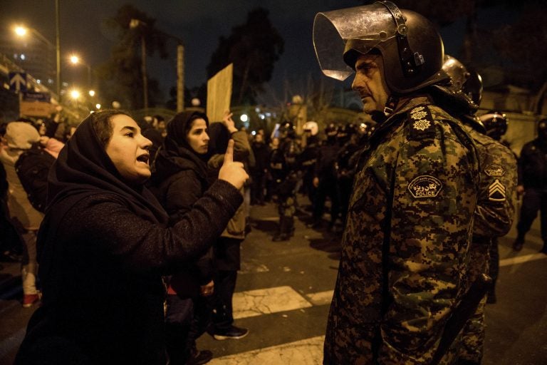 A woman attending a candlelight vigil to remember the victims of the Ukraine plane crash, talks to a policeman, at the gate of Amri Kabir University in Tehran, Iran.  (Mona Hoobehfekr/ISNA via AP)