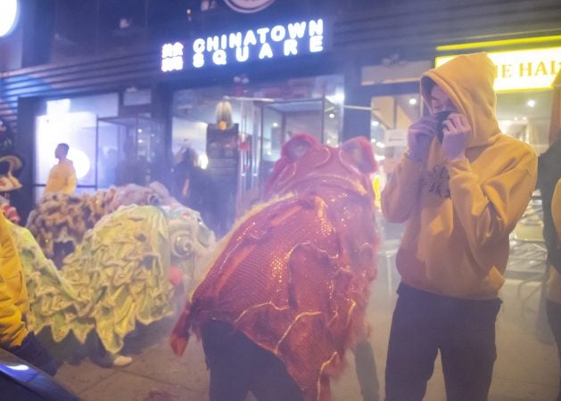 A member of the Philadelphia Suns Lion Dance group covers his mouth and nose as hundreds of fireworks explode around him. (Jonathan Wilson for WHYY)