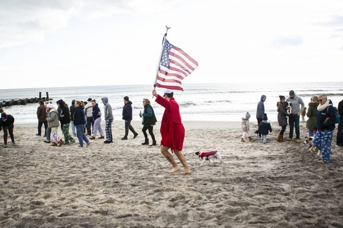 Teddy Costa run with a flag in front of the crow during the 2020 polar bear plunge in Margate, NJ on Wednesday, January 1, 2020. (Miguel Martinez for WHYY)