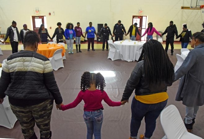 In November 2019, Tawanda Jones, leads attendees in prayer at the Michael J. Doyle Fieldhouse gym during a building shower to celebrate the Camden Sophisticated Sisters making a new home there.  (April Saul for WHYY)