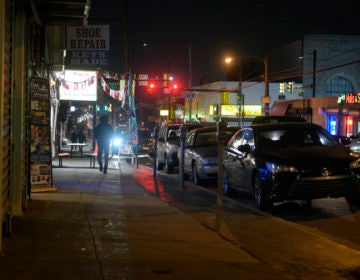 A street is shown at nighttime, with a few passersby walking by.