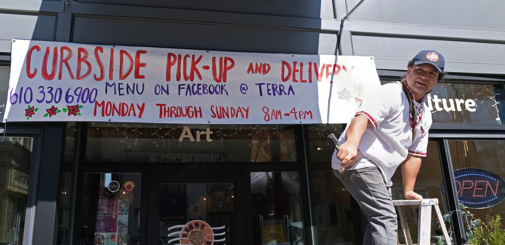 Terra Cafe co-owner Manuel Fresneda puts up a sign that advertises curbside pick-up and delivery for the Easton business. (Matt Smith for Keystone Crossroads)