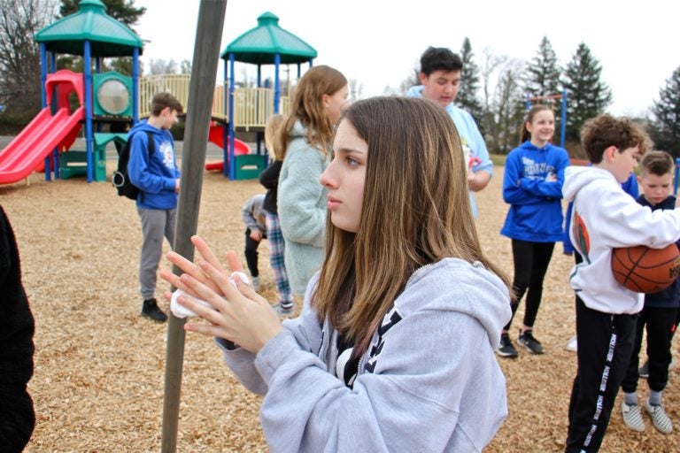 Tamanend Middle School student Brianna Muntz, 14,  uses a disposable hand wipe as she plays with friends on the Titus Elementary School playground. Both schools were closed, along with three others in Central Bucks County, as a precaution against the spread of COVID-19. (Emma Lee/WHYY)