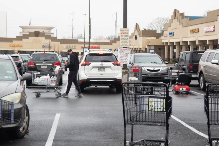 Carts litter the parking lot around 9 a.m. as a shopper heads back to their car with groceries after shopping at the ACME in Bala Cynwyd on March 19th 2020 during the uncertain times that surround the Covid 19 pandemic. (Emily Cohen for WHYY)