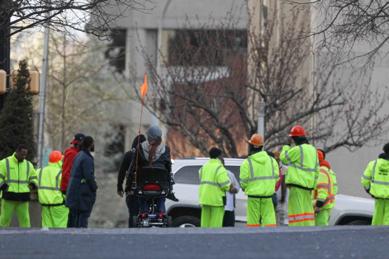 A pedestrian uses her scooter on Market Street in Wilmington, Del., as she approaches a group of construction workers on Thursday, March 26, 2020.  (Saquan Stimpson for WHYY)