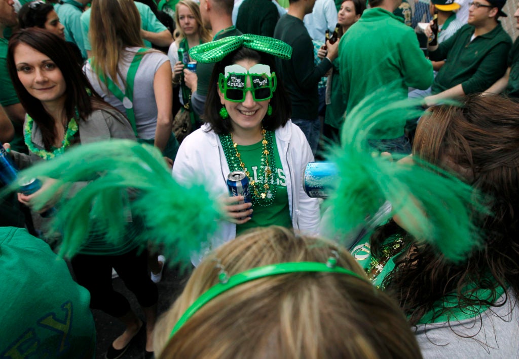 A woman stands in a crowd, wearing St. Patrick's Day glasses and other green accessories.