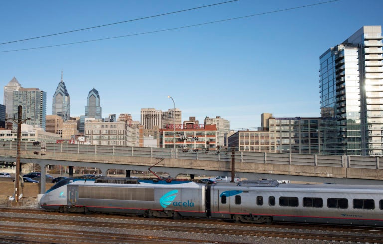 A train speeds by, as Philadelphia skyline is visible in the background.