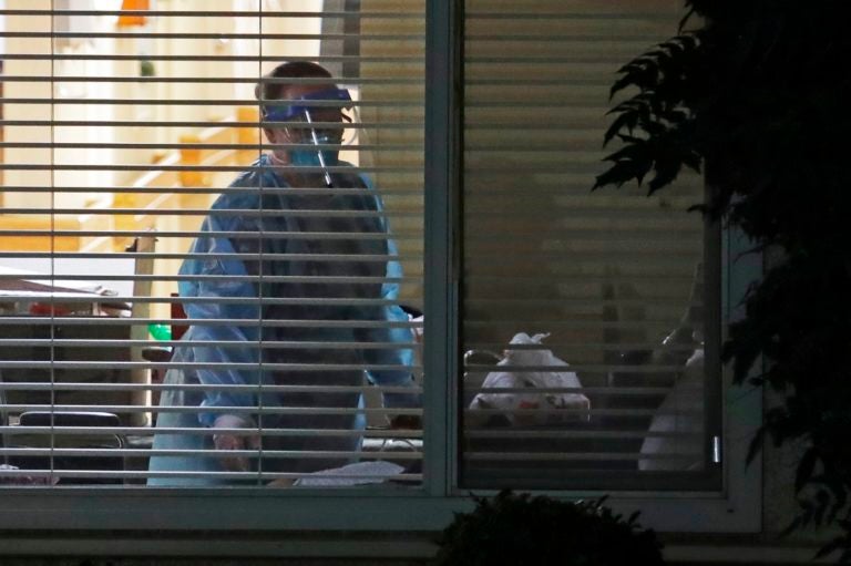 A worker wearing protective gear is seen through a window as she works in the room of Susan Hailey, 76, who has tested positive for the new coronavirus, Tuesday, March 10, 2020, at the Life Care Center in Kirkland, Wash., near Seattle. (AP Photo/Ted S. Warren)