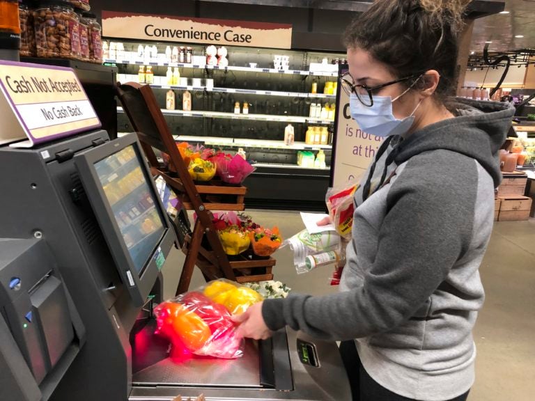 Wearing a surgical mask, Melissa Hall checks out of a Wegmans supermarket, Friday, March 13, 2020 in King of Prussia, Pa. (Michael Rubinkam/AP Photo)