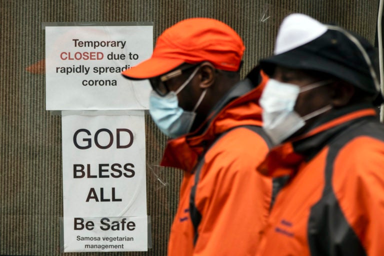 Pedestrians in protective face mask walk past a closed business in Philadelphia, Friday, March 20, 2020. (Matt Rourke/AP Photo)