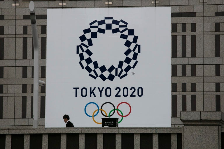 A man walks past a large banner promoting the Tokyo 2020 Olympics in Tokyo, Monday, March 23, 2020. The IOC will take up to four weeks to consider postponing the Tokyo Olympics amid mounting criticism of its handling of the coronavirus crisis that now includes Canada saying it won't send a team to the games this year and the leader of track and field, the biggest sport at the games, also calling for a delay. (AP Photo/Jae C. Hong)