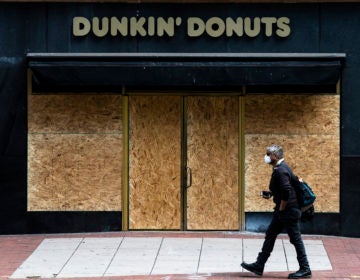 A person wearing protective masks due to coronavirus fears walks past a boarded up business in Philadelphia, Tuesday, March 24, 2020. (AP Photo/Matt Rourke)