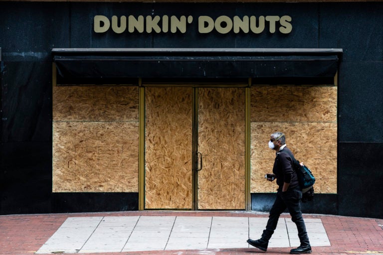 A person wearing protective masks due to coronavirus fears walks past a boarded up business in Philadelphia, Tuesday, March 24, 2020. (AP Photo/Matt Rourke)