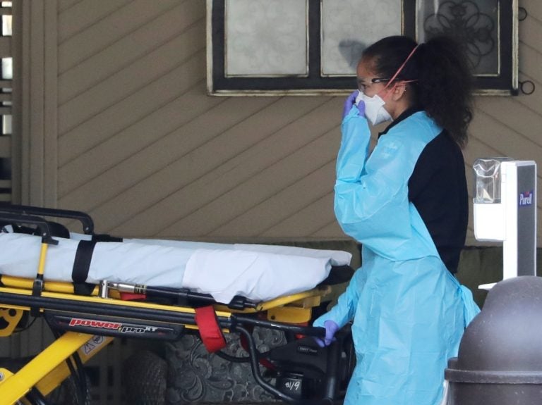An ambulance worker adjusts her protective mask as she wheels a stretcher into a nursing facility in Kirkland, Wash., on Saturday where more than 50 people were found to be sick and are being tested for COVID-19 virus. An ambulance worker adjusts her protective mask as she wheels a stretcher into a nursing facility in Kirkland, Wash., on Saturday where more than 50 people were found to be sick and are being tested for COVID-19 virus. (Elaine Thompson/AP Photo)