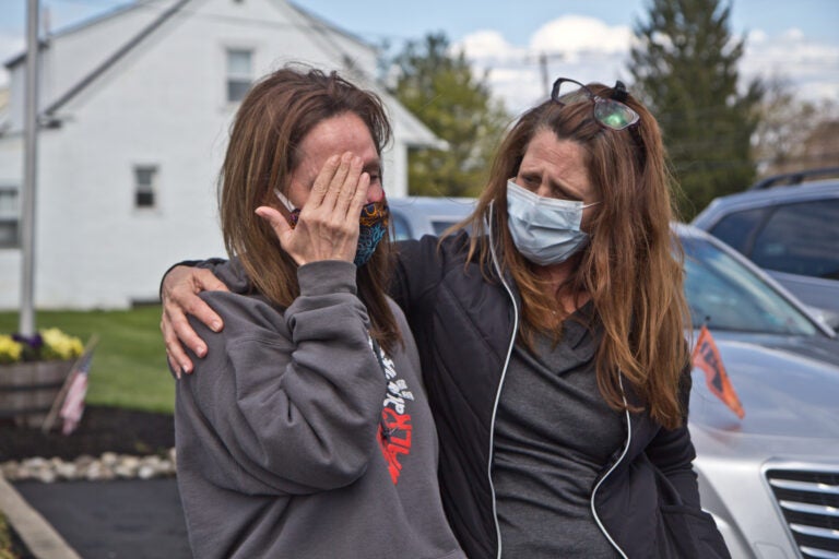 Tammy King (left) is comforted by her sister Michelle Rouco, both nurses, who were not allowed to see their father before he succumbed to COVID-19. (Kimberly Paynter/WHYY)