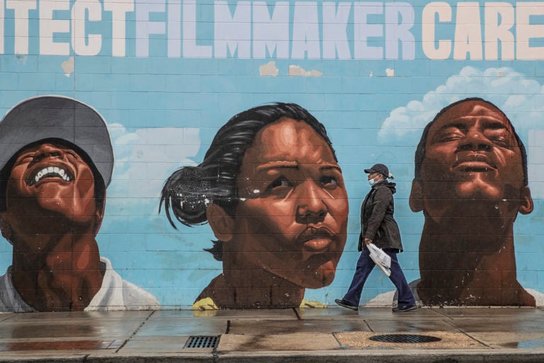 A woman wearing a surgical mask makes her way past a mural on the west side of the Save-A-Lot store at 22nd and Lehigh. (Michael Bryant/The Philadelphia Inquirer via AP)