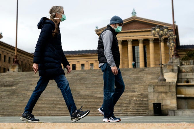 A couple in protective masks walk past the Philadelphia Museum of Art in Philadelphia, Friday, April 3, 2020.