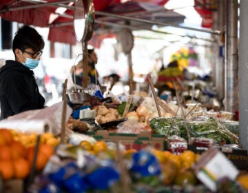 A vender wearing a face masks to protect against the spread of new coronavirus, works at a produce stand on South 9th Street in Italian Market neighborhood of Philadelphia, Thursday, April 9, 2020. (Matt Rourke/AP Photo)