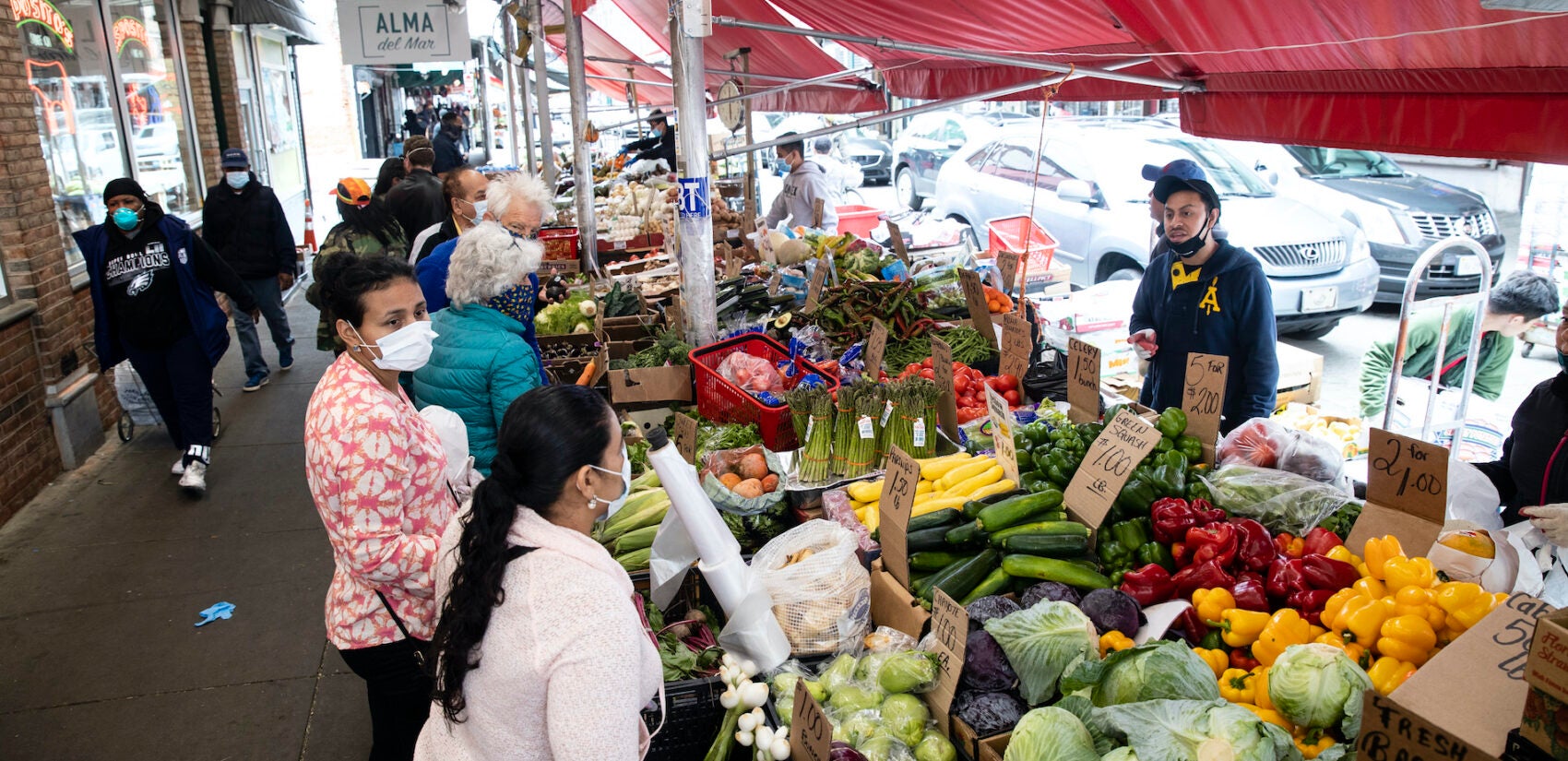 Customers wearing face coverings to protect against the spread of the coronavirus, shop at a produce stand on South 9th Street in the Italian Market neighborhood of Philadelphia, Thursday, April 9, 2020. (AP Photo/Matt Rourke)