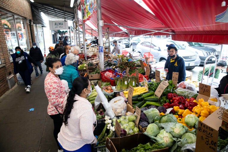 Customers wearing face coverings to protect against the spread of the coronavirus, shop at a produce stand on South 9th Street in the Italian Market neighborhood of Philadelphia, Thursday, April 9, 2020. (AP Photo/Matt Rourke)