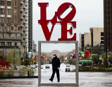 A person wearing a protective face mask and gloves as a precaution against the coronavirus walks through Love Park, in Philadelphia, Monday, April 13, 2020. (Matt Rourke/AP Photo)